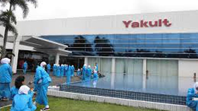 Ilustrasi gedung dan produk Yakult Indonesia yang sedang membuka kesempatan karir bagi para pencari kerja profesional maupun fresh graduate.